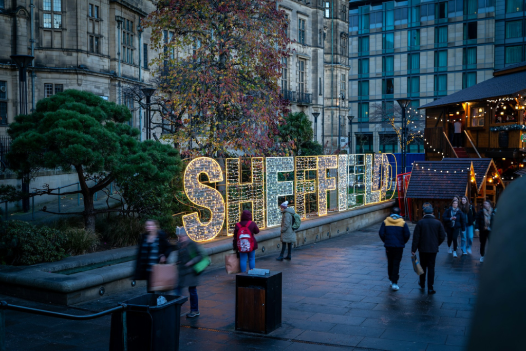 Late night image of Peace Garden in Sheffield with neon Sheffield sign and people walking past