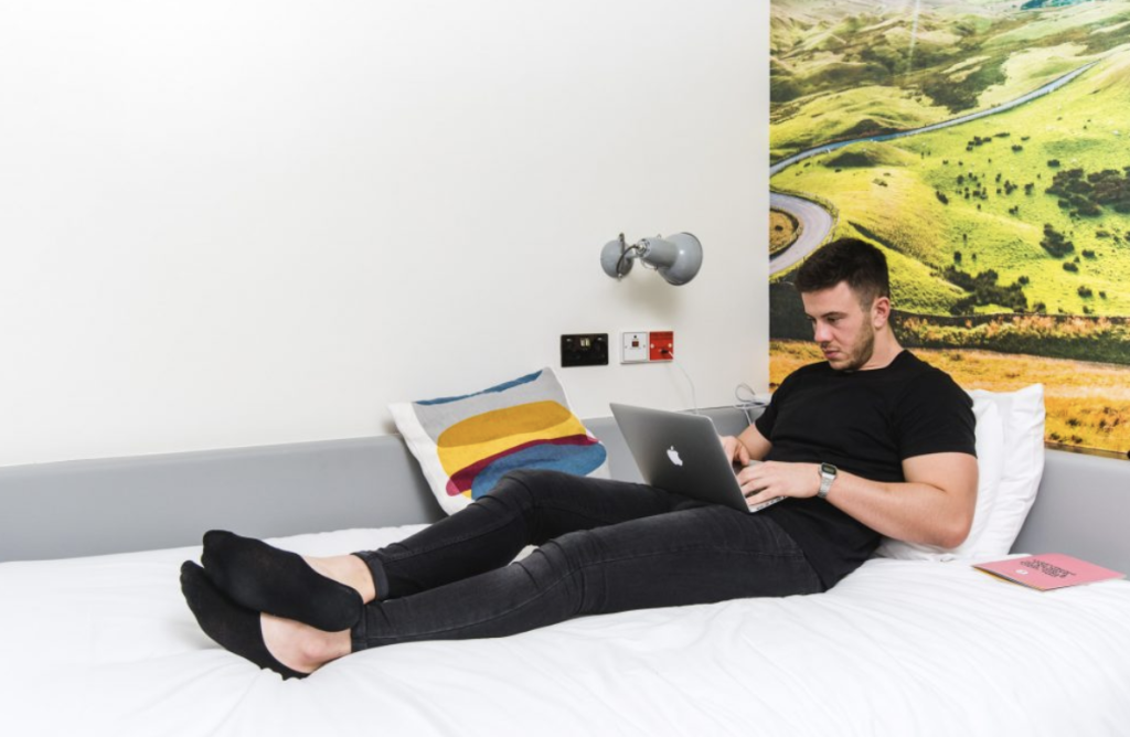 Man sat on a laptop working while sat on a bed in a hotel room at Jonas Hotel Sheffield